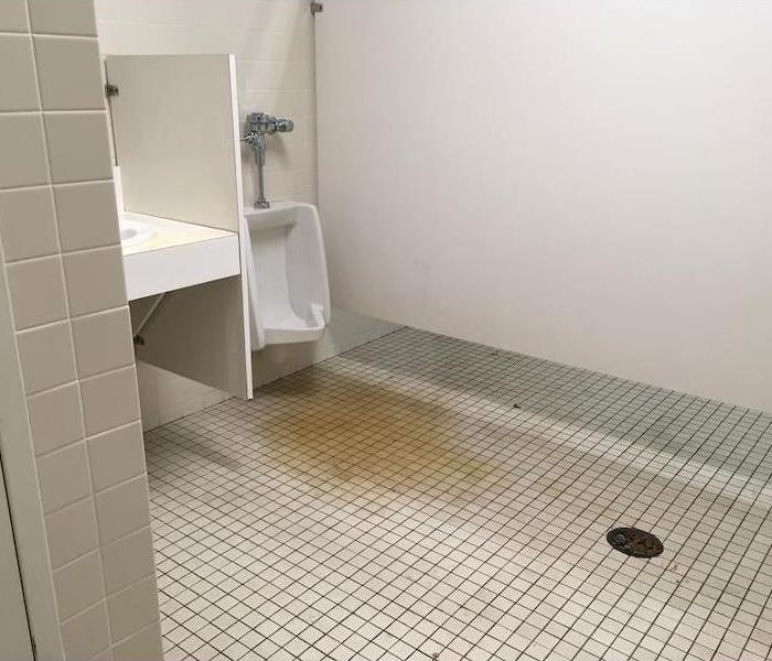 Commercial bathroom with white tile and stain on the floor