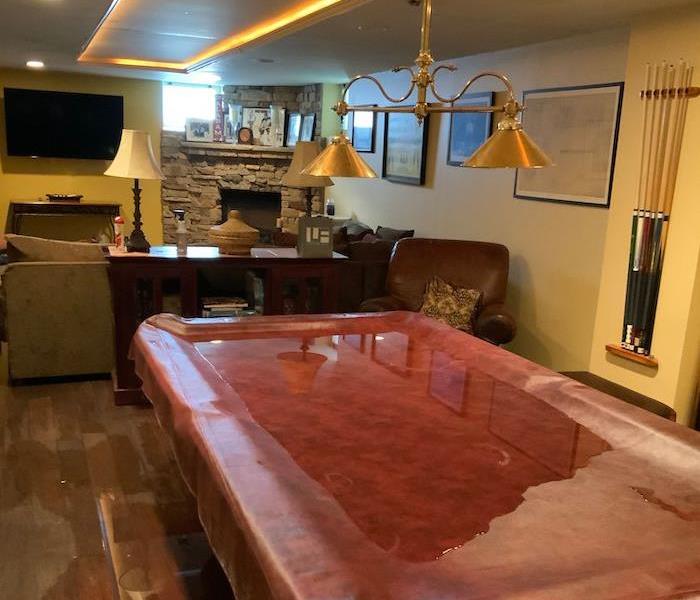 Pool table cover on hardwood floor with standing water