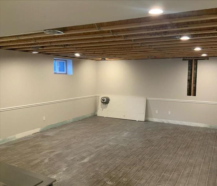 Basement at a similar angle to the Before Photo with removed furnishings, baseboards, and ceiling drywall