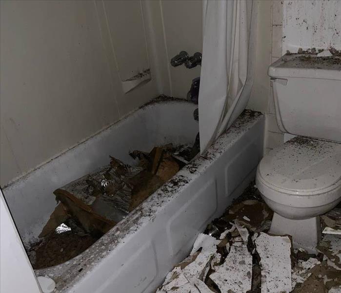 White bathtub with ceiling debris in tub and on floor