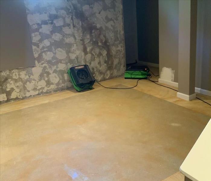 SERVPRO drying equipment on a bare basement floor with the sheetrock on a single wall removed